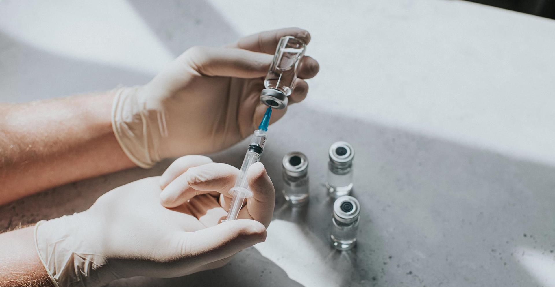 Gloved hand holds a syringe and a phial - Conceptual medical image with space for copy.