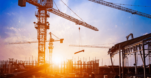 Silhouetted construction cranes against a vibrant sunset.