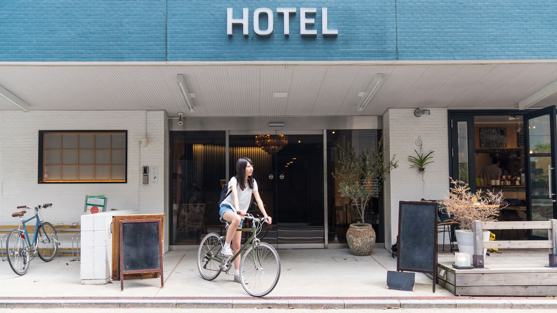 Junge Frau auf einem Fahrrad vor einem Hotel - Klimaneutralität in der Hotelbranche