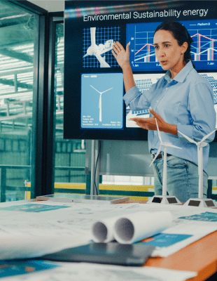 A diverse group of professionals engaged in discussion in a meeting room, with a large screen displaying information.