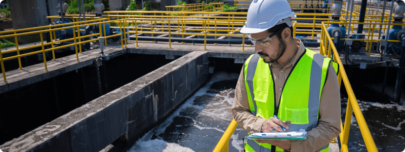A man in a hard hat and safety vest writes on a clipboard, ensuring safety protocols are followed.