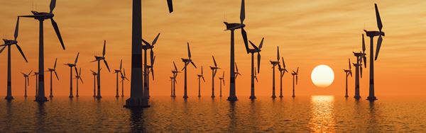 Wind turbines stand tall in the ocean at sunset, creating a striking contrast against the vibrant hues of the sky.