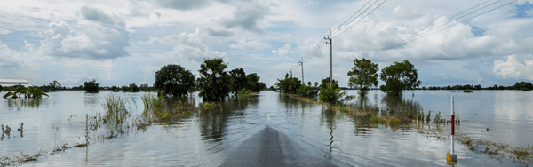 Flooded road surrounded by lake that reflects the natural surroundings and a cloudy sky.