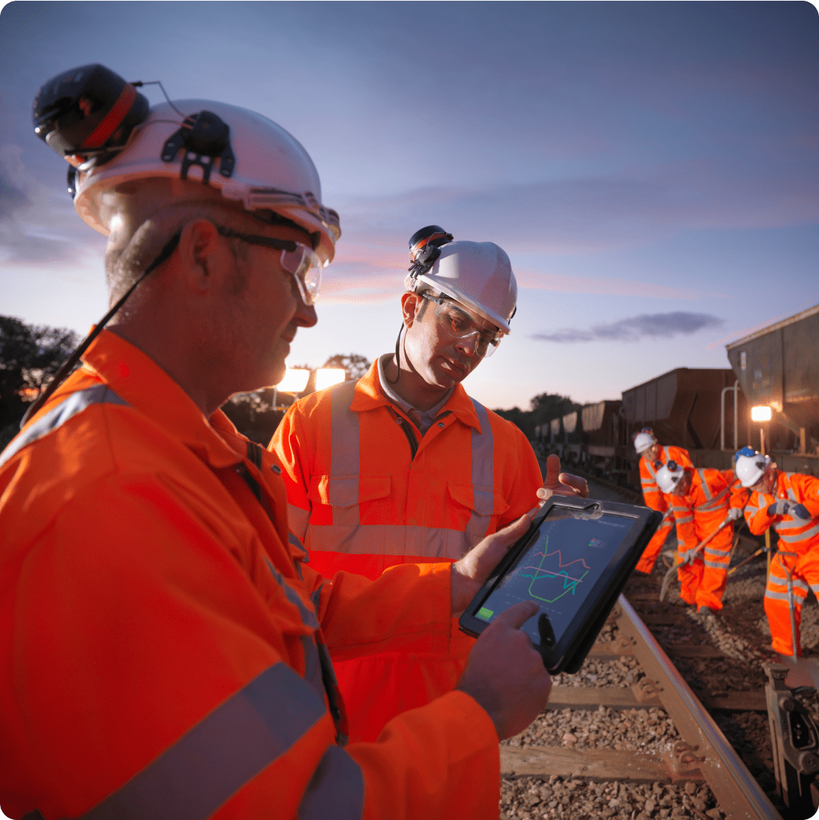 Two individuals dressed in orange safety attire are engaged with a tablet, assessing information together.