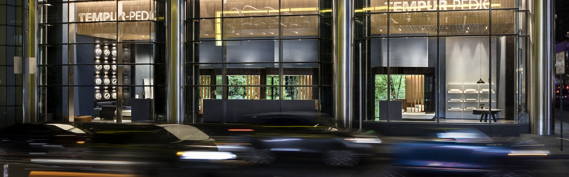 A city building with cars passing by at night, illuminated by street lights.