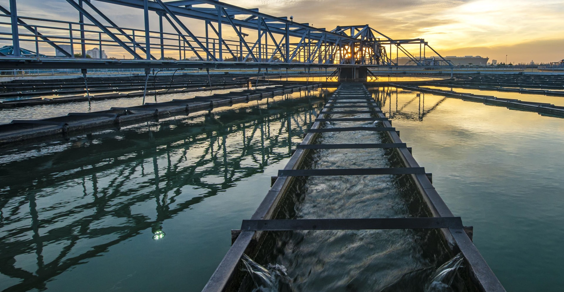 Sunset view of a water treatment plant, featuring large tanks and pipes.