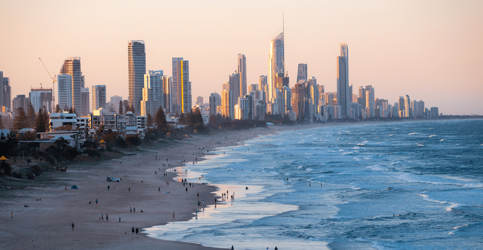 A lively beach populated with individuals relaxing on towels, children playing in the sand, and others swimming in the ocean.