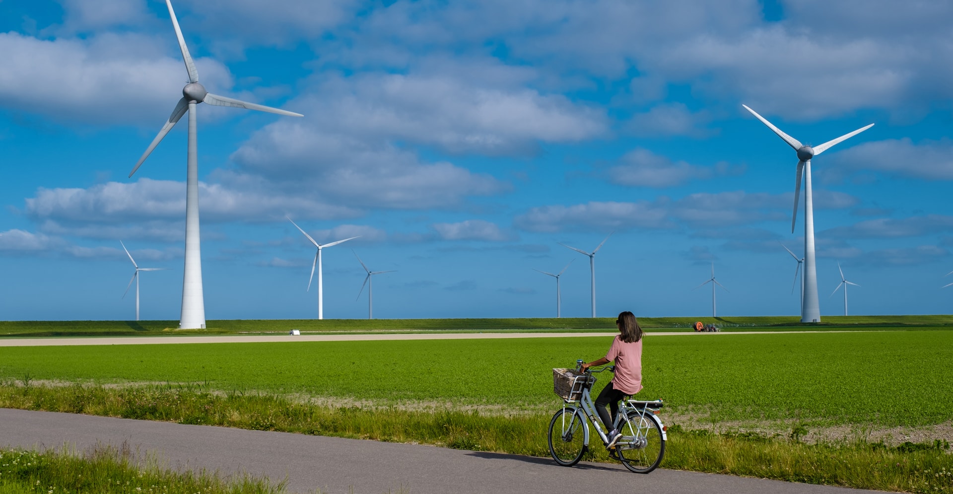 young woman electric green bike bicycle by windmill farm, windmills isolated on a beautiful bright day Netherlands Flevoland Noordoostpolder