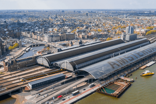Aerial drone view of the historic Amsterdam Centraal station building and platforms situated along the IJ river waterfront in the Netherlands.