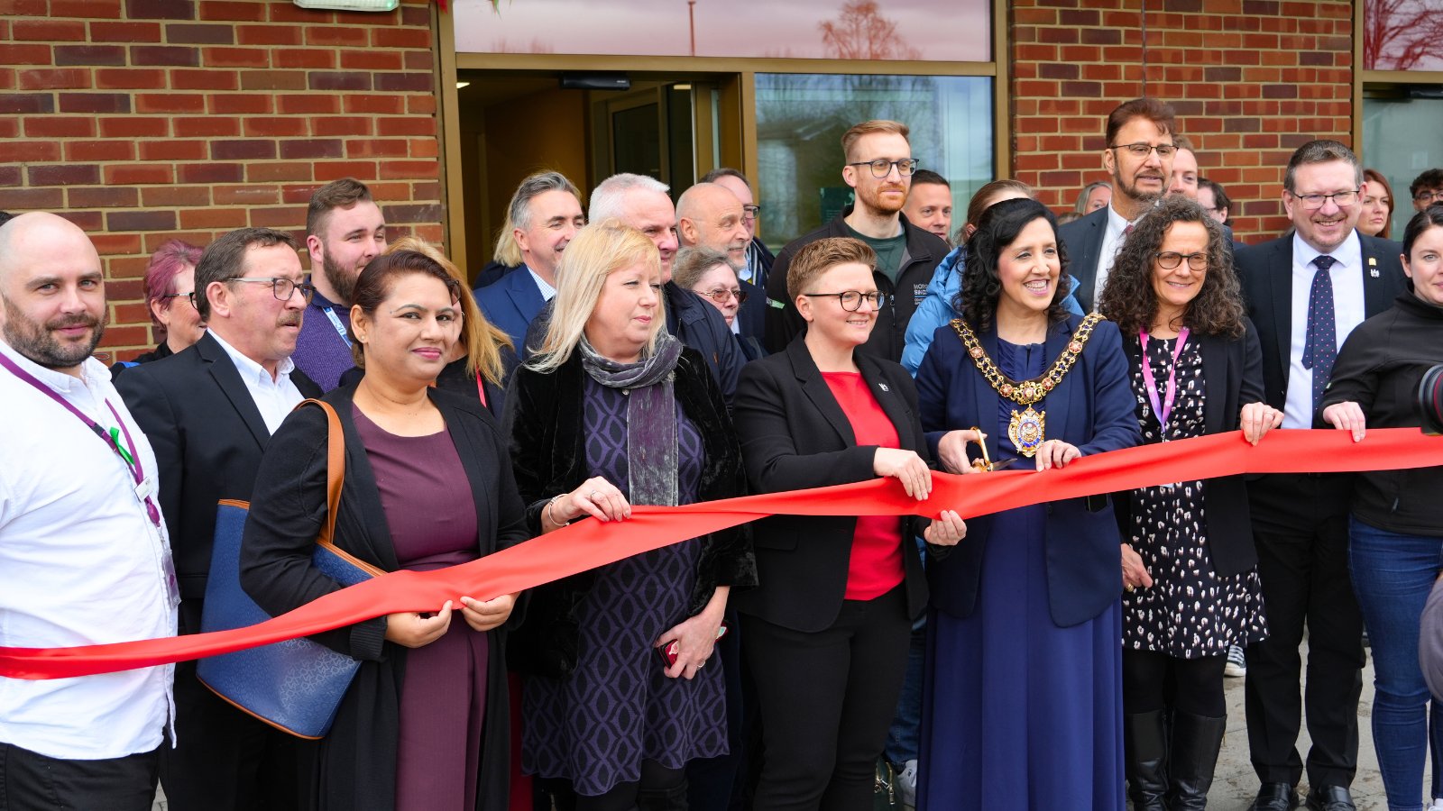 A group of people joyfully cutting a ribbon of Gorton Hub inauguration ceremony.