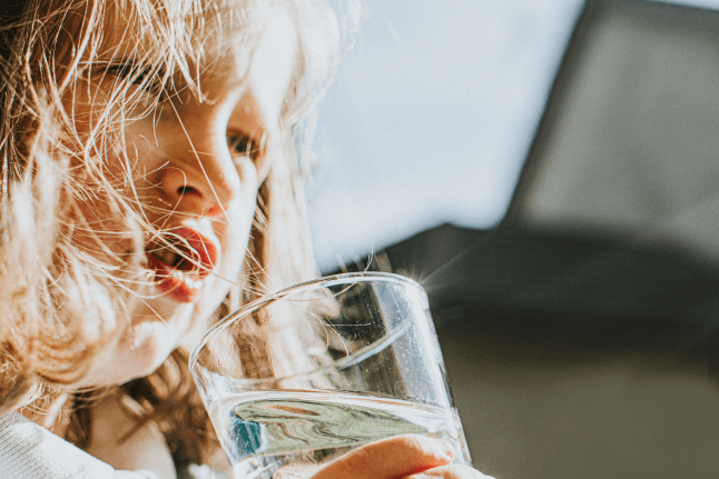 A young child holding a clear glass of clean drinking water under bright sunlight.