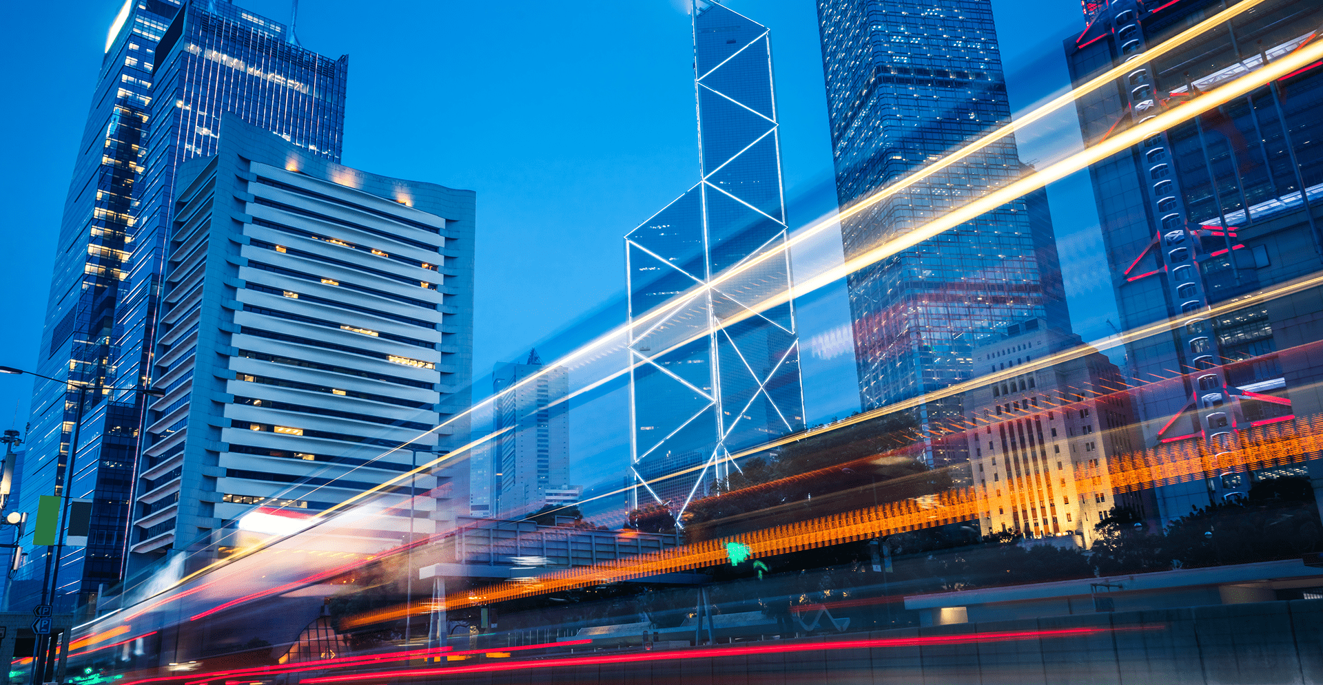 Cityscape at dusk with modern skyscrapers and light trails from passing vehicles in the foreground.