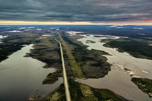 Aerial view of a highway curving alongside a body of water, showcasing the landscape's natural and man-made features.
