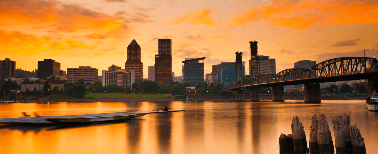 A vibrant city skyline silhouetted against a colorful sunset, with buildings outlined in warm hues of orange and pink.