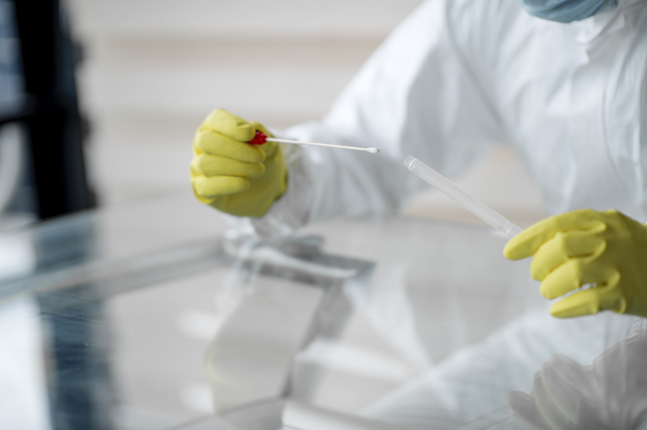 Person in medizinischem Schutzanzug mit Teströhrchen für Corona-Test