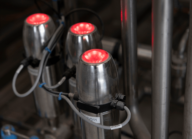 Three metal pipes with red lights glowing, captured in a close-up view, highlighting their sleek and modern appearance.