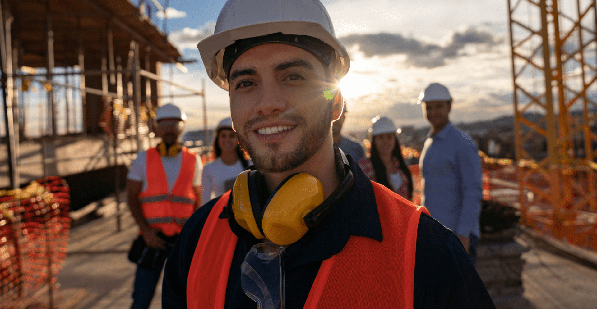 A man in a hard hat stands confidently, ready for work in a construction or industrial environment.