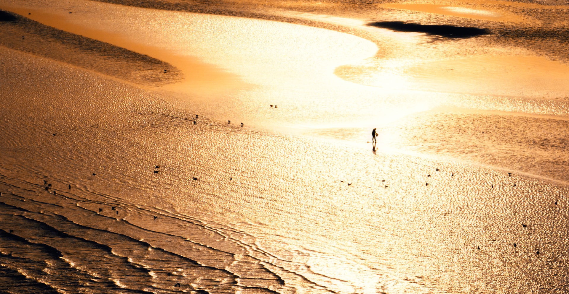 A person walks along a sandy beach with waves gently crashing in the background.