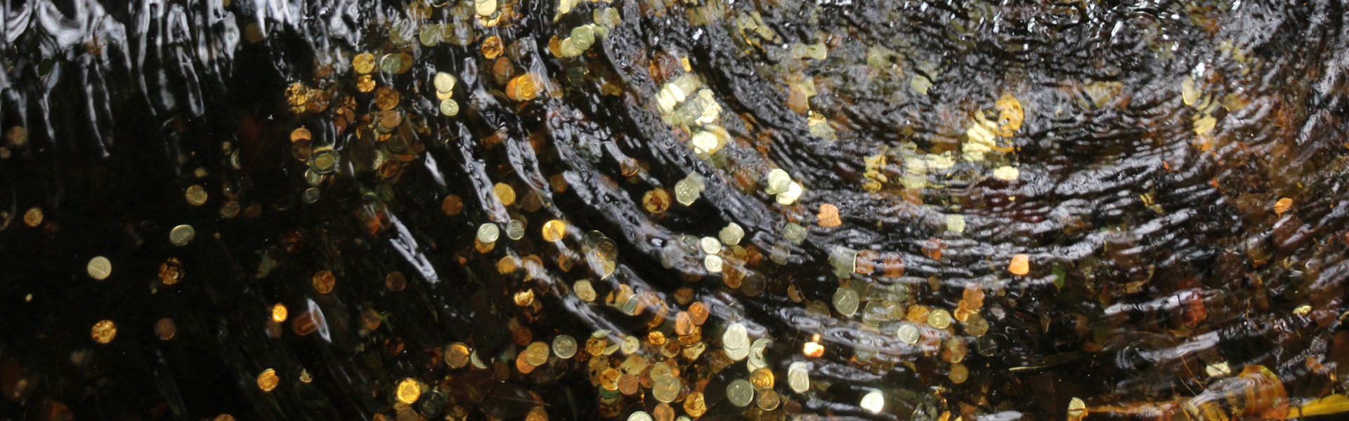A close-up view of a waterfall cascading over rocks, with shimmering gold coins scattered among the flowing water.