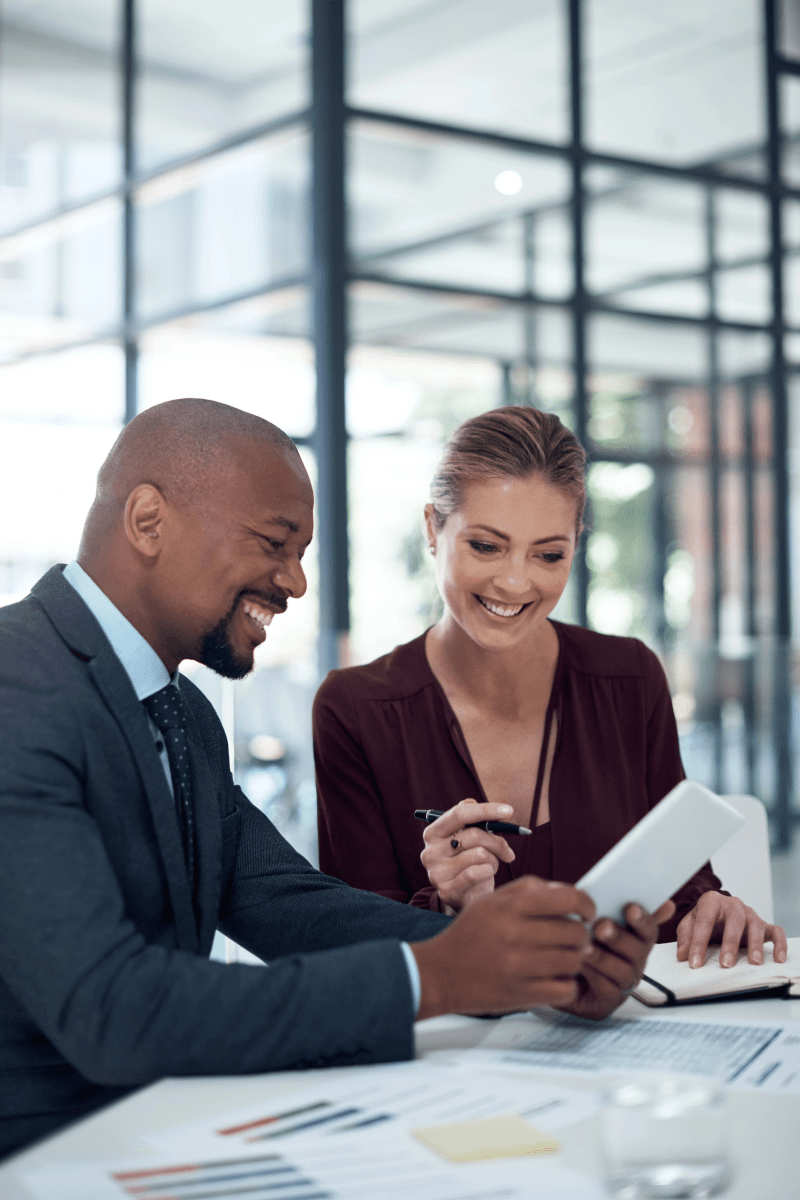 A pair of business individuals seated at a table, actively using a tablet to facilitate their meeting and exchange ideas.