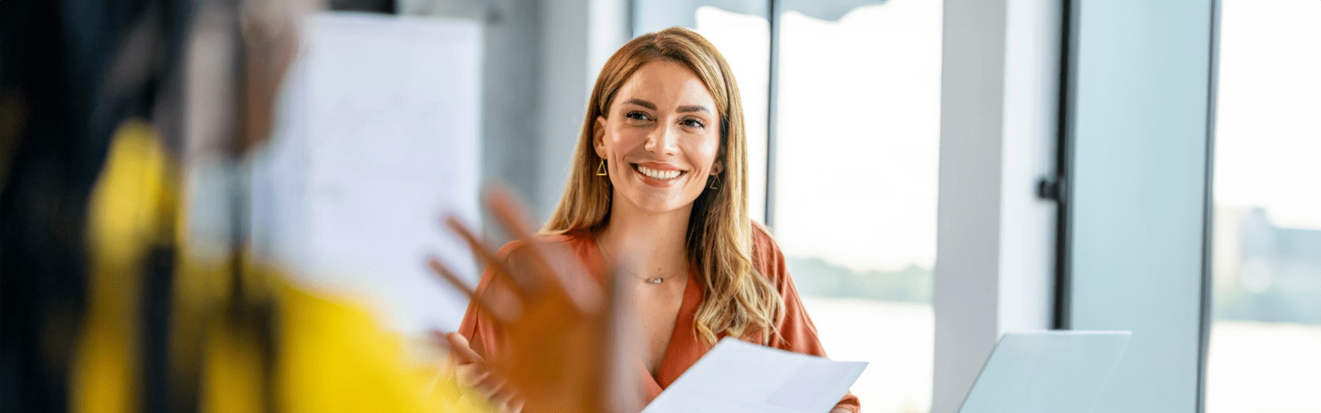 A woman with a bright smile sits in a conversation, embodying a moment of joy and concentration.