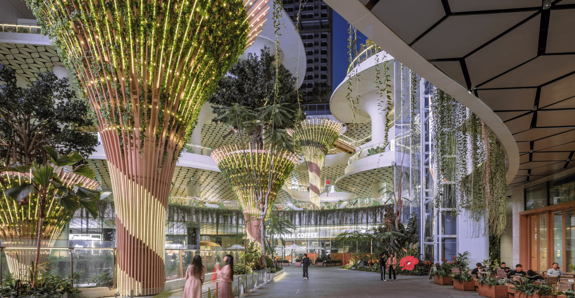 The atrium features lush trees and plants, creating a vibrant indoor garden atmosphere within the building.