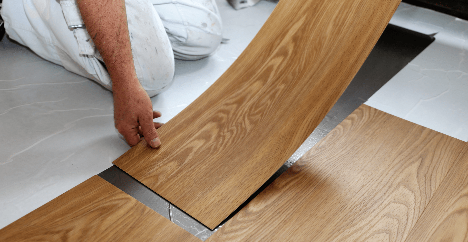  A man is in the process of installing wood flooring, highlighting his focus and dedication to achieving a flawless finish.
