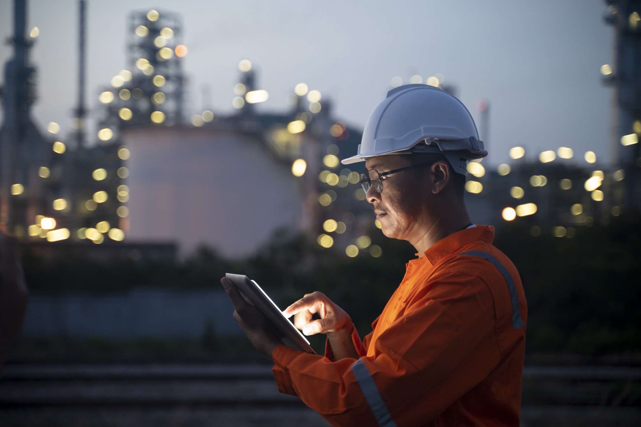Ingenieur mit Tablet in der Nähe von Ölraffinerie in der Dämmerung