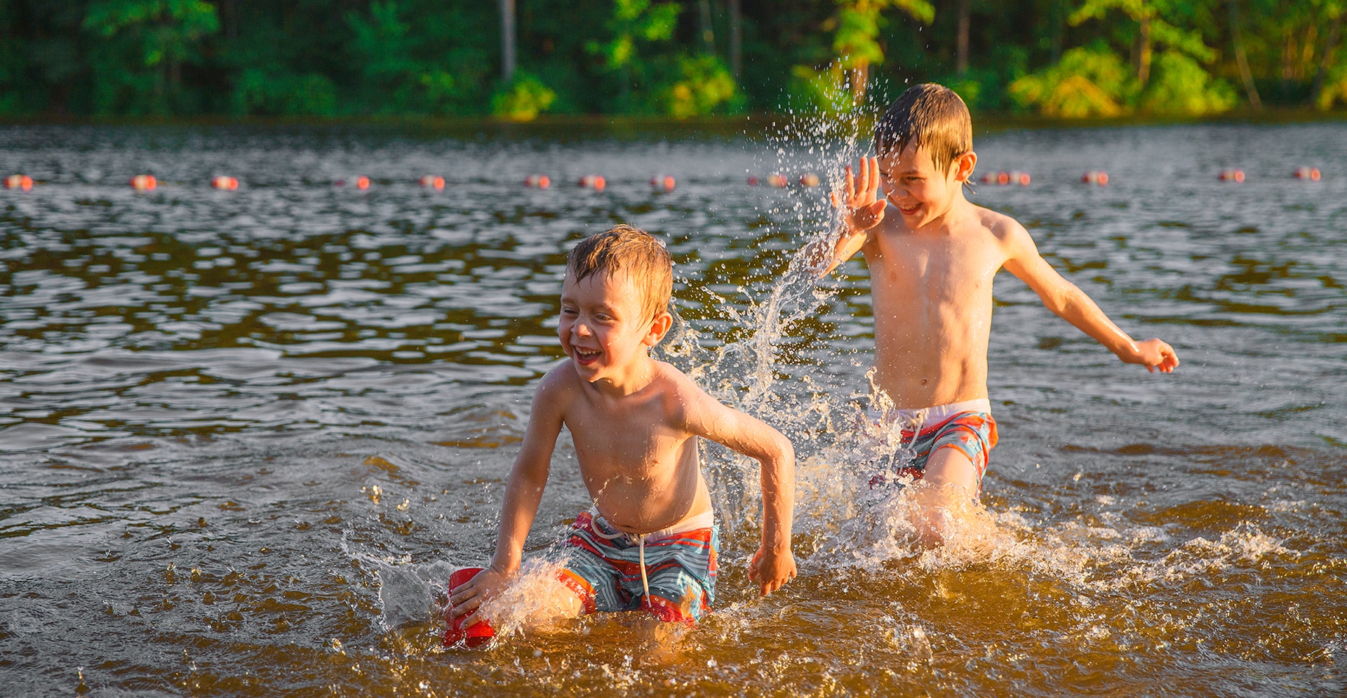 Twee jongens rennen elkaar in het water achterna.