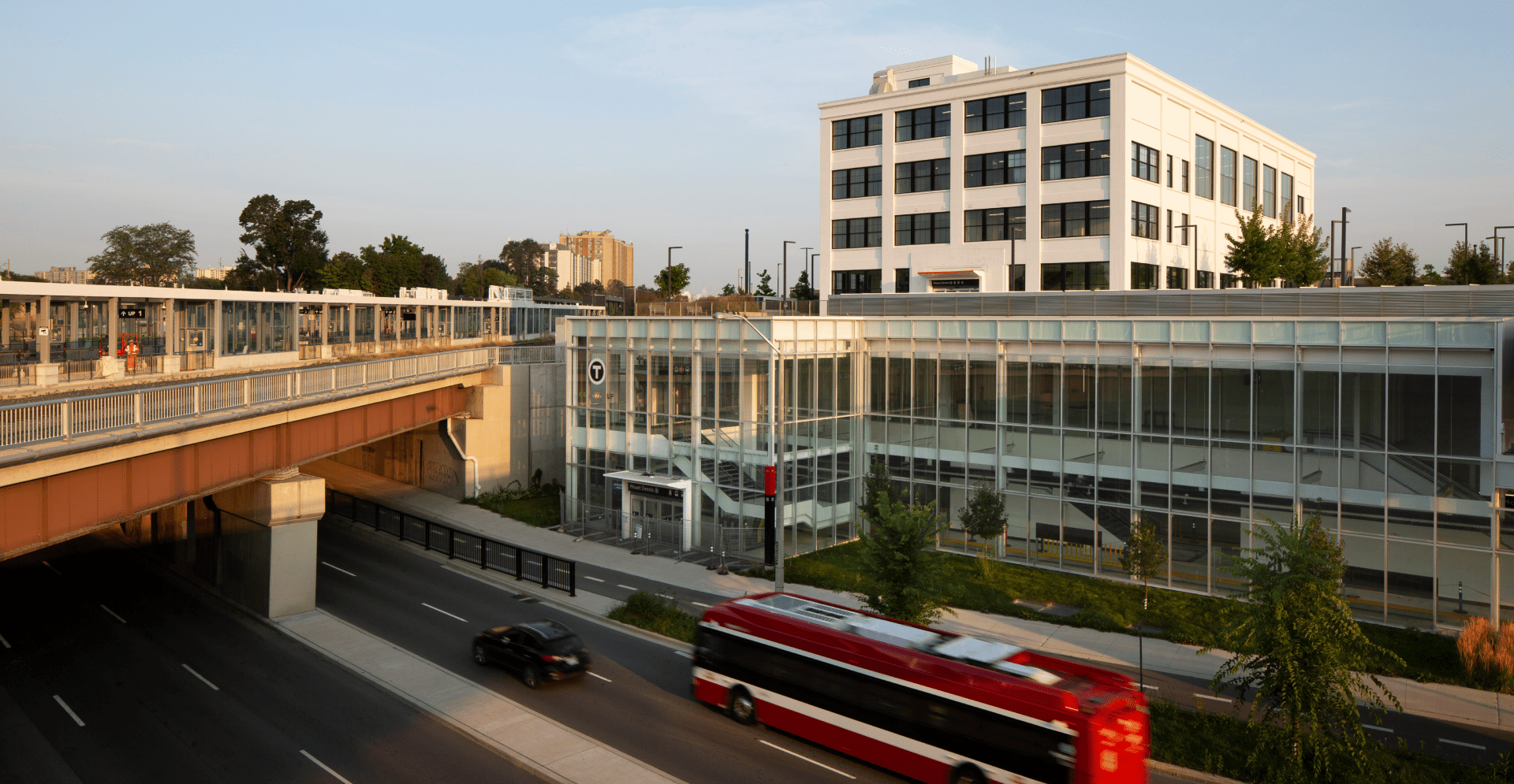 A red bus travels along a highway beside a building under a clear sky.