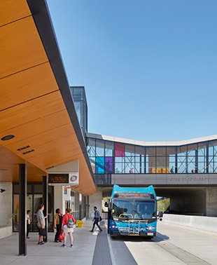 A bus is parked at a bus stop adjacent to a building, ready to pick up passengers.