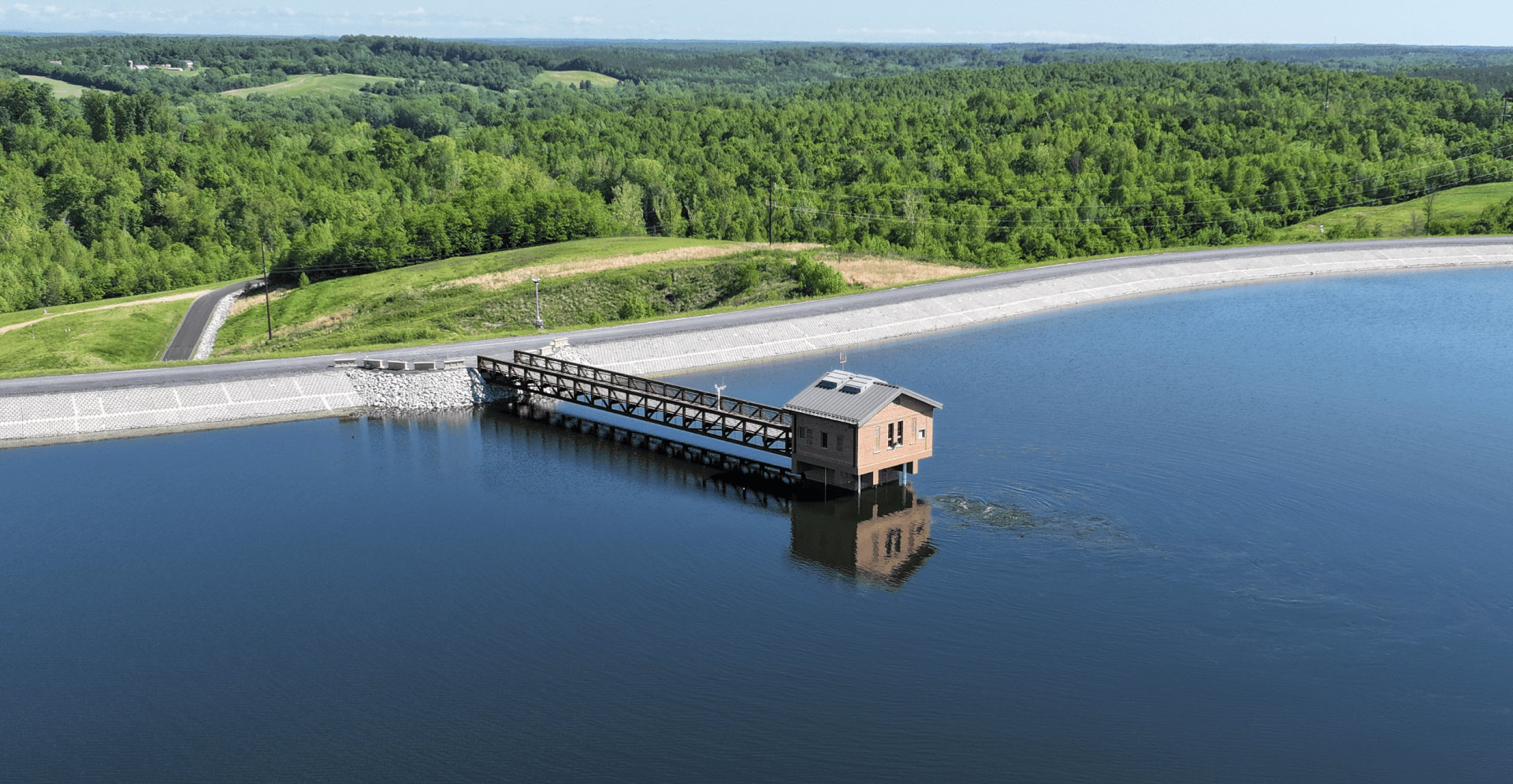 A dam on a serene lake, encircled by lush green trees, reflecting nature's tranquility.