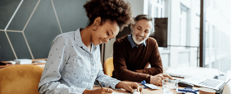 A man and woman seated at a table, reviewing documents and discussing details together.